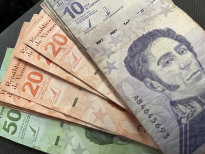 The image shows a fan of Venezuelan banknotes, primarily featuring denominations of 10, 20, and 50 bolivars. The banknotes are laid out on a dark, textured surface, likely fabric. The details visible on the bills include the text "República de Venezuela," numerical denominations, dates, signatures, and portraits. There is no visible indication of the city of Conuco Viejo, Venezuela.