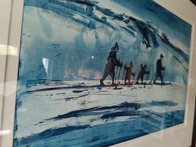 This is a framed print depicting a snowy, mountainous landscape in Hovden, Norway. Four figures, dressed in winter clothing and carrying ski poles, are skiing across a vast, snow-covered plain. The style is painterly with broad brushstrokes in shades of blue and white, creating a sense of depth and movement in the snow. Dark, abstract shapes in the upper portion of the print suggest rugged mountain peaks, possibly covered in snow or shadowed. The scene evokes a feeling of isolation and the stark beauty of a winter environment. The time of day is unclear, but the lighting suggests it could be daytime. A handwritten inscription is visible along the bottom edge of the print, partially obscured by the frame.