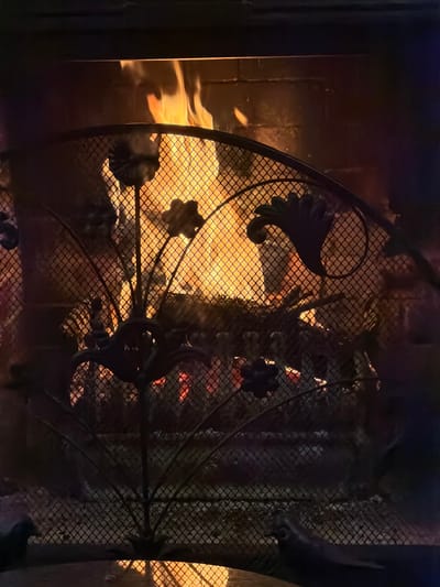 The image shows a fireplace with a decorative metal grate in front. The grate has floral-like designs. Behind the grate, flames are visible. The scene is dark, illuminated by the firelight. There is no information about the location of Кирково, Bulgaria within the picture.
