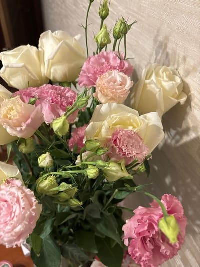 A bouquet of flowers, predominantly pink and white roses with green buds, is arranged in a vase against a textured, beige wall. The lighting suggests an indoor setting, casting shadows on the wall. There are no people or observable actions taking place. The specific location within Otradnoye, Russia cannot be determined from the visual information provided.