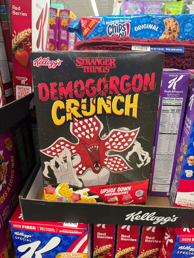 The image shows a grocery store shelf in North Brunswick Township, United States, stocked with various Kellogg's cereal boxes. The most prominent item is a box of "Stranger Things Demogorgon Crunch" cereal, featuring the Demogorgon monster from the television show "Stranger Things". Surrounding it are boxes of Kellogg's "Red Berries" cereal, "Special K Fruit & Yogurt" cereal, and "Special K Strawberries" cereal. A blue "Chips Ahoy!" cookie box and a small bath rug are visible behind the cereal boxes.