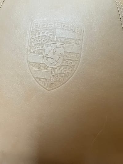 The image shows a close-up of a light tan surface, likely leather or a similar material, embossed with the Porsche crest. The crest features a horse at its center, surrounded by the word "STUTTGART" and other heraldic elements, all rendered in a slightly lighter shade than the background material. The surface appears to be part of a car interior, potentially a seat or dashboard. There are no people visible in the image. The image does not have information about Blajievo, Bulgaria.