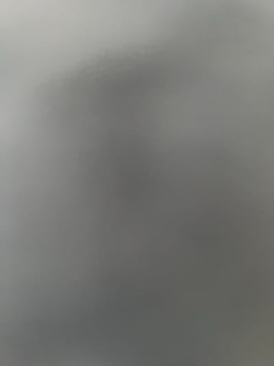 The image is a blurry, abstract photograph of a gray surface. There are no discernible objects, people, or actions depicted. The lighting is diffuse and the focus is soft, creating a muted and indistinct visual. The overall impression is one of formlessness and lack of detail.