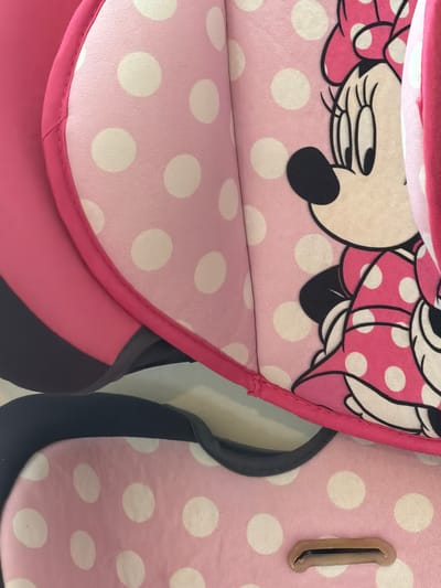 The image shows a close-up of a child's car seat featuring a pink polka-dot design and Minnie Mouse details. No people, identifiable locations within Bearpark, or actions are depicted. The scene is limited to the car seat's material and design elements.