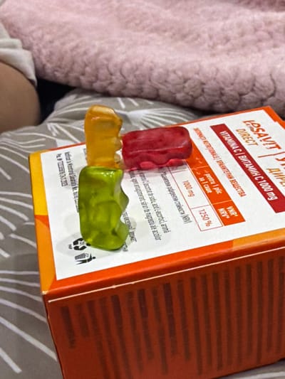 The image shows a box of "Losavit Direct Vitamina C 1000 mg" alongside three gummy bears. The gummy bears are red, yellow, and green, and are resting on the box. The text on the box includes information such as "pentru 1 plic/za 1 саше" (for 1 sachet), "1000 mg", and "1250% VNR/NRV". The image also includes text in Bulgarian. Based on the ingredients listed, it is probably a vitamin C dietary supplement.