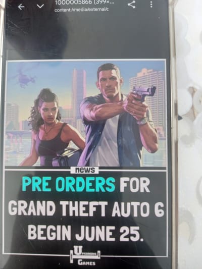 A screen display shows an advertisement for Grand Theft Auto 6. The advertisement features an image of two characters, a man and a woman, in front of a city skyline. The man, with short dark hair and a beard, is wearing a blue shirt and holding a handgun. The woman, with dark curly hair pulled back, is wearing a black tank top and a necklace, and is carrying a black bag. A helicopter is visible in the sky behind them. The text on the screen reads "news PRE ORDERS FOR GRAND THEFT AUTO 6 BEGIN JUNE 25." A logo for "UPCOMING GAMES" is at the bottom. The screen display itself shows minor scratches and appears to be a photograph of a mobile device. There is no information within the image that relates to the city of Oshane, Bulgaria.