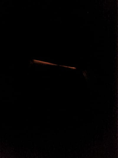 The image depicts a dark, possibly night, scene with a faint orange light streaking horizontally across the center. This light appears to be a long exposure effect, possibly from a vehicle or train passing by. The environment is predominantly black, with some faint granular texture visible, suggesting a low-light photograph with some noise. There are no discernible people, specific objects, or clear environmental features like buildings or landmarks that would allow for precise identification of the location within Solingen, Germany. The overall impression is one of movement captured in darkness.