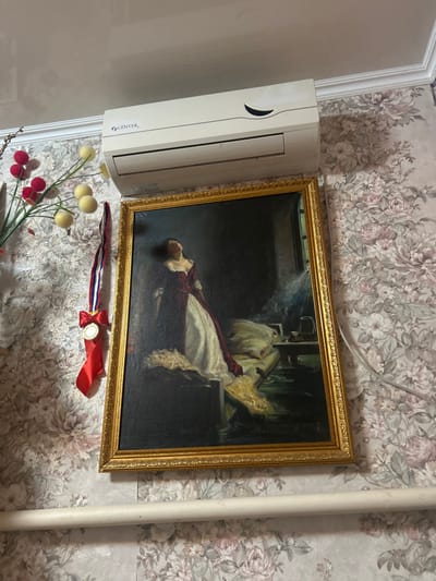 This image depicts an interior wall within a room in Dmitriyevskaya, Russia. A white "CENTEK" brand wall-mounted air conditioning unit is positioned prominently near the ceiling. Below it, a large, vertically oriented oil painting with an ornate gold frame hangs on the wall. The painting illustrates a woman in a red and white period gown, her head tilted upwards, standing beside a bed in a dimly lit room with a window to her right. To the left of the painting, a decorative floral arrangement featuring red and yellow spherical elements is visible. Below this arrangement, a medal with a red, white, and blue striped ribbon and a red bow is suspended from the wall. The room's walls are covered in wallpaper with a repeating pattern of large, muted floral designs. A white horizontal pipe or baseboard runs along the lower portion of the wall. The ceiling is white and a white crown molding separates it from the wallpaper.