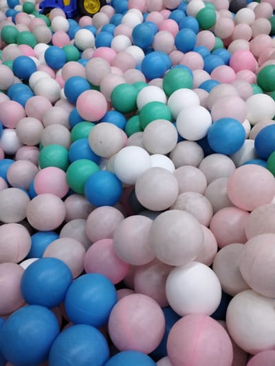 The image shows a pile of colorful plastic balls in a ball pit, likely at a children's play center. The balls are predominantly pink, blue, and white, with some green and other muted colors mixed in. The lighting suggests an indoor environment. There are no people visible in the image. The scene is static and focuses solely on the texture and arrangement of the balls. The location in Talas City, Kyrgyzstan, is not visually discernible from the image itself.