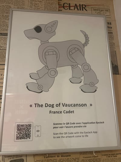 This image depicts a framed poster displayed on a wall in Cucuron, France. The poster, vertically oriented and encased in a light metallic frame, features an illustration of a stylized, grey, robotic dog with black eyes and segmented limbs, joints, and a coiled tail. The dog is presented in a standing or walking posture, facing left. Below the illustration, the text reads "« The Dog of Vaucanson »" and "France Cadet." In the lower left corner, a QR code is visible next to a small graphic of a smartphone screen displaying a red lip icon. Accompanying text, in both French and English, instructs viewers to "Scan the QR Code with the EyeJack App to see the artwork come to life." The wall behind the poster is covered entirely with aged newspaper clippings, revealing headlines such as "ECLAIR" and a date stamp indicating "Samedi 13 Mars 1948." No individuals, explicit actions, or direct interactions are captured in the scene.