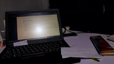 The image presents a laptop on a white desk in Umuigbekwo, Nigeria, with a document open titled "Statement 1: Plan of Study" for the Queen Elizabeth Commonwealth Scholarship. The document outlines questions to be addressed in the statement, such as course choice, university preference, career relevance, and candidate suitability. A sticky note on the keyboard displays "Username = Email All, Password ***" and a link to a job posting for South African Antiquities (SAQA) evaluation. A smartphone lies next to the laptop, and a small notebook sits beside it. The environment appears to be a dimly lit indoor setting.