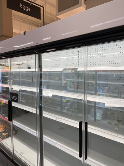 The image shows an empty refrigerated display case in a supermarket. The case is located in the city of Middle Park, Australia, at coordinates -27.556 latitude and 152.923 longitude. It is a glass-fronted case with multiple shelves, containing no products. There are multiple rows of small black circles on the exterior of the case, likely air vents. There are two black handles that open the case. There is a sign above the case that says "Eggs" and a sign near the bottom of the case that reads "On sale this week - buy 2 get 1 free." There are several other signs visible on the case but their contents are illegible.