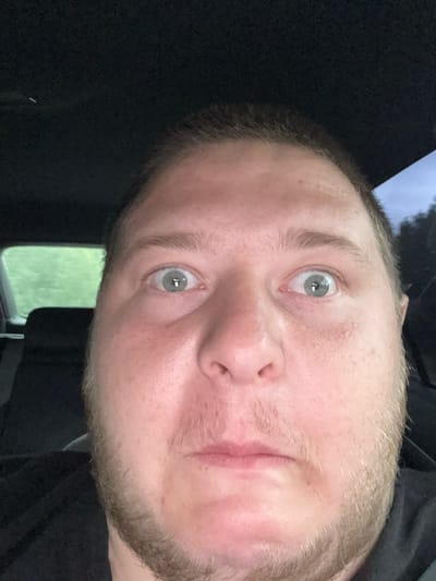 A close-up, tilted selfie of a light-skinned man with light eyes and stubble. He appears to be inside a vehicle. A window with greenery visible outside is in the background. The location of Mezdreya, Bulgaria, is not discernible from the visual information available.