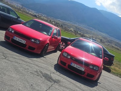 The image shows two red Volkswagen Golf R32 cars parked on an asphalt surface. The license plates on both cars are "CO 1644 CT" and "CO 1644 CX" respectively, indicating they are likely registered in the Sofia region of Bulgaria. A black car is partially visible behind each of the red cars. The background features a mountainous landscape and what appears to be the city of Kraynitsi in Bulgaria. The lighting suggests it is daytime with clear skies.