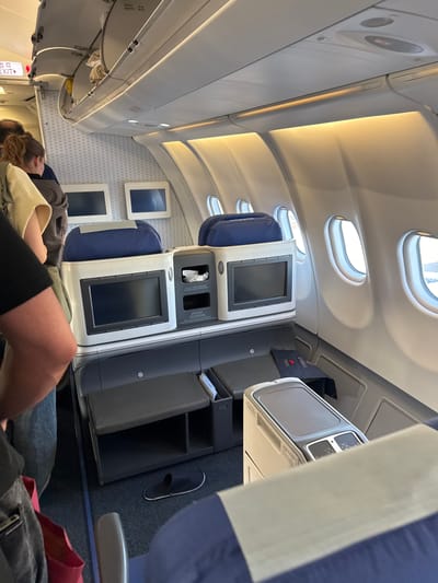 The image appears to be taken inside the business class section of an airplane. Passengers are visible in their seats, and personal entertainment screens are present in front of each seat. Windows along the plane's side are also visible. The image doesn't provide specific details that would allow for identification of Stolbishche, Russia.