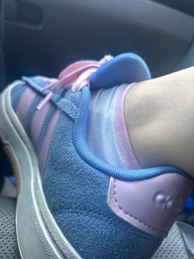 A close-up shot shows the side of a light blue and pink Adidas shoe with pink laces. The shoe is on a person's foot, with the ankle and part of the leg visible. The background is dark and out of focus, suggesting the photo was taken indoors, possibly in a vehicle. The scene appears to be located in Sammamish, United States of America.