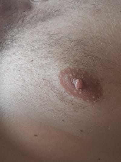 The image shows a close-up view of a human nipple and areola, with surrounding skin and fine hairs. The areola is a light brown, circular area with a slightly darker, raised nipple protruding from its center. The nipple appears to have small bumps or papillae on its surface. The skin around the nipple is lighter in tone and covered in sparse, light-colored hairs. The overall lighting suggests an indoor setting with soft illumination. There is no context provided regarding the location in the city of Таёжное, Russia.