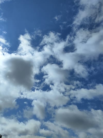 The image depicts a sky with a mix of blue sky and scattered white and gray clouds. The clouds are varying in size and density, with some appearing wispy and translucent, while others are thicker and more opaque, casting shadows. The lighting suggests it is daytime, with sunlight illuminating the clouds. The scene is entirely composed of the sky, with no discernible ground features or urban elements visible. The provided context of Lāņi, Latvia, suggests this is an outdoor scene in that location.