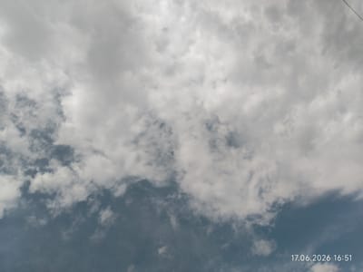 This is a close-up, upward-facing shot of a cloudy sky. The clouds are a mix of white and gray, with some areas appearing brighter than others, suggesting varying thicknesses and light penetration. The lower portion of the sky transitions to a darker, more muted blue-gray, indicating either deeper cloud cover or a shift in atmospheric conditions. The overall impression is of a dynamic sky, possibly with changing weather. The lighting suggests it is daytime, with the sun likely behind some of the denser cloud formations. There are no visible people or objects, and the scene is solely focused on the sky. A thin, dark line, possibly a wire or a thin branch, is visible in the upper right corner, extending diagonally downwards. In the bottom right corner of the image, the text "17.06.2026 16:51" is visible, indicating the date and time the photograph was taken.