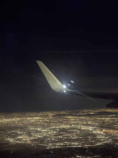 An aerial night photograph displays the right wing and an illuminated, upward-curving winglet of an aircraft in the mid-ground and foreground. Bright white navigational or strobe lights are active on the wing and winglet, casting visible illumination. Below the aircraft, a vast, dense expanse of diffused golden-yellow artificial lights covers the ground, depicting a large metropolitan area. This illuminated urban landscape is identified as the region of Rancho Palos Verdes, United States. The upper portion of the image is a dark, starless night sky. No individuals or specific subjects beyond the aircraft components and city lights are discernible. The scene records an aircraft's perspective during nighttime flight over an expansive, lit urban environment.