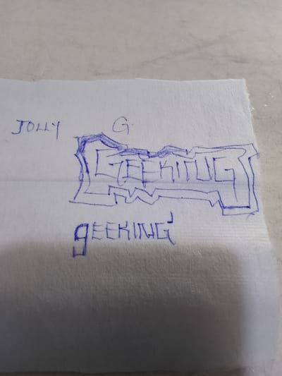 The image displays a close-up, slightly angled view of a white paper towel with blue ink markings. On the left side of the paper towel, the word "JOLLY" is written in cursive. To the right of "JOLLY," a single letter "G" is written. In the center of the paper towel, a stylized drawing of the word "GEEKING" is outlined in bold blue ink. Below this central drawing, the word "GEEKING" is written again in simpler, block-like blue letters. The paper towel is resting on a textured, light-colored surface. There is no discernible information in the image that would relate it to Rumuepirikom, Nigeria, or any specific urban location.