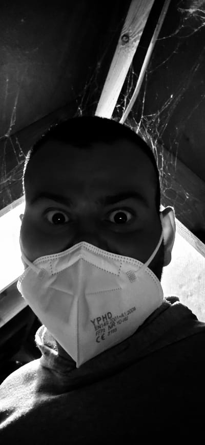 A black and white, low-angle photograph shows a person wearing a white medical-style face mask. The mask has the text "YPHD" printed on it, along with other lettering and symbols. The person's eyes are wide and looking up at the camera. The background appears to be an interior space, possibly an attic or crawlspace, with wooden beams and what appears to be cobwebs. There is no confirmed information about the location of this picture being in Barntrup, Germany.