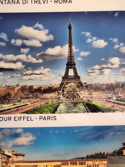 The image shows a postcard featuring two distinct scenes. The top half depicts the Eiffel Tower in Paris, France, set against a bright blue sky with scattered white clouds. The tower is a prominent, dark brown lattice structure with a pointed top. Below the tower, a cityscape with buildings and trees is visible, along with a reflective body of water and grassy areas. The text "TOUR EIFFEL - PARIS" is printed below this image.

The bottom half of the postcard shows a view of a European city, likely Florence, Italy, with its distinctive Renaissance architecture. Buildings with terracotta roofs and arched windows line a canal or river. In the background, a hilly landscape dotted with trees and some buildings can be seen.

There is no information in the image that links it to Bochum, Germany. The scene is entirely focused on Parisian and Italian landmarks.