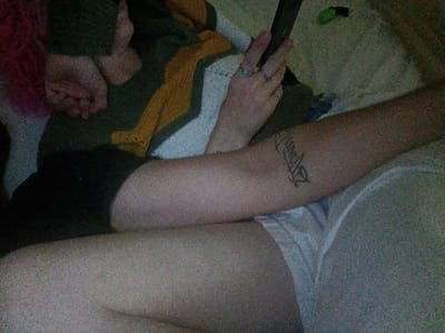 A person is lying on a gray surface, presumably a bed. The individual is wearing black shorts and white underwear. Their left arm is resting on the surface, displaying a tattoo. Their right hand is held up, showing two fingers extended in a V shape. The location in Fort Smith, United States of America, is not discernable from the image.