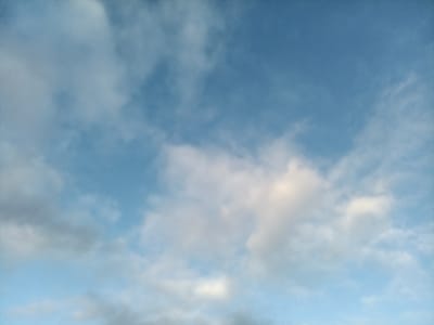 A daytime sky fills the frame with a mix of blue and white. The sky is predominantly blue, interspersed with fluffy, white clouds. Some clouds are dense and opaque, while others are thin and wispy. The lighting suggests diffused sunlight, casting soft shadows within the cloud formations. Overall, the image presents a tranquil and airy atmosphere.