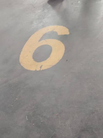 The image shows the number "6" painted in yellow on a grey concrete surface. The paint is slightly worn and chipped. The surface appears to be a floor in an indoor or outdoor location, possibly a parking lot or industrial area. There are no people or other distinguishing features in the image. The location of Потапово, Russia is not evident from the image itself.