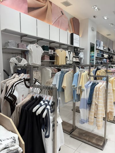 The image depicts the interior of a clothing store, likely in Dagupan, Philippines. The scene is filled with rows of apparel neatly displayed on shelves and hanging racks. The subjects are primarily clothing items, including t-shirts, sweaters, and possibly pants, in various colors like yellow, white, blue, pink, and brown.
The store appears well-lit, with artificial lighting from overhead fixtures casting a bright glow on the merchandise. The setting is clean and organized, suggesting a retail environment focused on presenting clothing attractively to customers. There is no visible activity of people shopping or working in the immediate frame, implying the photo was taken when the store was either closed or empty.
Notable details include the arrangement of clothing by color and type, and the presence of price tags or labels on some items. One sign is clearly visible, reading "DRESS CODE" in bold letters. The overall impression is one of a contemporary retail space, possibly a boutique or a section within a larger department store. The time of day and weather are not discernible from the image.