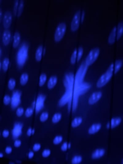 The image shows a dark blue surface illuminated with blurred blue lights. The lights are arranged in a pattern, with some appearing as small circles with what look like three dots inside, and one larger shape that resembles a star. The surface appears to be textured, possibly with horizontal lines or ridges. The lighting gives the scene a nocturnal or interior atmosphere. The Borino, Bulgaria location is not confirmed by the image alone.