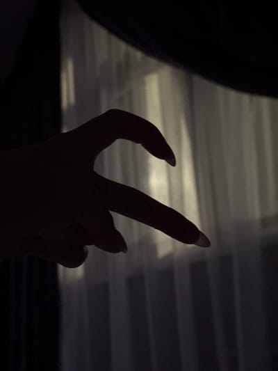 In the city of Doma 1096 Km, Russia, a close-up, silhouette photograph captures two hands forming a heart shape. The hands, positioned in the foreground, are silhouetted against a softly lit backdrop of vertical blinds. The left hand is curved inwards, with its thumb and index finger forming the top curve of the heart. The right hand's index finger extends and meets the curve of the left hand, completing the heart shape. The lighting creates a dramatic contrast, casting the hands in deep shadow while the blinds are illuminated by an unseen light source, suggesting an indoor setting with a window. The overall impression is one of intimacy and connection, conveyed through the gesture of the hands.
