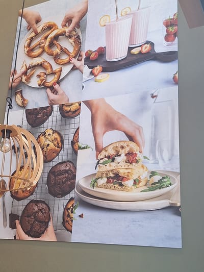 The image is a collage of food-related photographs. In the top left, several hands are arranging pretzels on a white plate. To the right, two pink smoothies with banana slices are shown in glasses, with a pile of strawberries in the background. Below the smoothies, a wooden cutting board with more strawberries and banana slices is visible. In the bottom half of the image, a rack of muffins is shown, with a wooden light fixture in the foreground. To the right of the muffins, a hand is placing a halved sandwich filled with white cheese, red tomatoes, and green leaves onto a plate. The overall aesthetic suggests a collection of culinary or recipe photographs. There is no discernible information within the image that indicates a location in the city of Bochum, Germany.