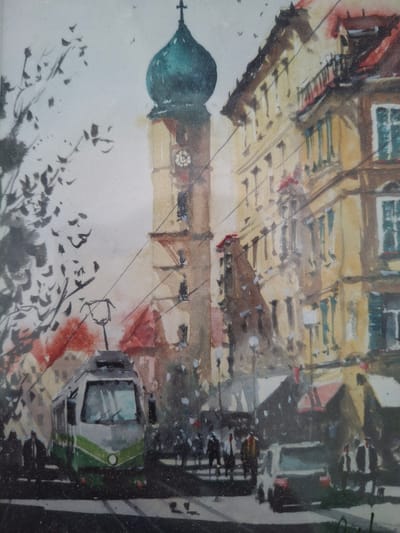 This is a watercolor painting of a city street scene, likely depicting Graz, Austria, given the architectural style and the presence of a tram. The focal point is a tall clock tower with a green, onion-shaped dome, topped with a cross. To the right of the tower are multi-story buildings with yellowish facades, red roofs, and numerous windows, some with green shutters. In the foreground, a modern tram with green and white accents is prominent. Several indistinct figures of people are visible on the sidewalk and crossing the street, suggesting a busy urban environment. A white car is parked on the right side of the street. The left side of the painting features the silhouette of a tree with dark, sparse branches against a light sky, with a few small bird figures in flight. The overall style is impressionistic, with visible brushstrokes and a somewhat muted color palette. The scene appears to be set during the daytime.