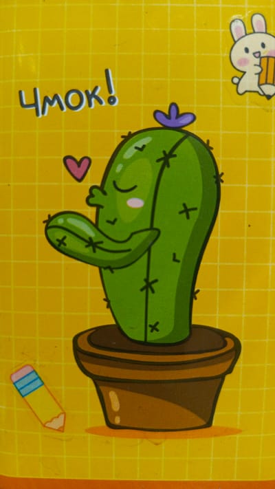 The image displays a cartoon of a cactus in a pot on a yellow, grid-patterned background. The cactus is green, with closed eyes and blushing cheeks, and has a purple flower on its head. It is also shown to be puckering its lips, as if to give a kiss, with a pink heart above its left arm. To the left of the cactus is a cartoon of a pencil with a pink eraser and blue and yellow segments. In the top right corner, there is a cartoon of a white rabbit holding a pencil. Above the cactus, the Cyrillic word "ЧМОК!" is written in large, dark letters, which translates to "Mwah!" or "Kiss!". There are no identifiable landmarks or elements in the image that would indicate a specific location in Zvenigorod, Russia.