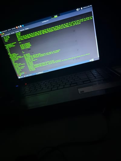 This is a close-up, angled shot of a laptop screen displaying a command-line interface, likely in a dimly lit room. The screen shows various system information and security-related text, predominantly in green font against a dark background. The date and time displayed on the screen are "16:03, Jun 25, Thu".
The command-line interface appears to be from a Linux-based operating system, possibly Parrot OS, given the username "ivallo@parrot". Text such as "CPU max MHz", "CPU min MHz", "BogoNIPS", "Flags", and "Virtualization features" suggest a system information report. There are also sections detailing "Vulnerabilities" and "Mitigations", indicating a security scan or analysis is being performed. Some of the listed vulnerabilities include "Spectre v2", and mitigations like "Retpolines" and "Split huge pages" are mentioned.
The keyboard of the laptop is partially visible, suggesting the image was taken from the perspective of someone sitting in front of the laptop. The overall mood is dark and focused, emphasizing the technical content on the screen. There are no people visible in the frame, and the setting appears to be indoors. The location context of Dalgopol, Bulgaria, is provided externally but not visually evident from the image itself.