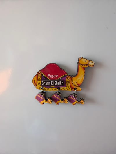 A refrigerator magnet shaped like a camel with a saddle reads "Egypt Sharm El Sheikh". Below the main camel are three smaller camel-shaped magnets. The magnet is attached to a plain, light-colored surface, likely a refrigerator door. There are no people or discernable actions occurring in the image. The environment appears to be indoors, with soft lighting. The location of the image in Dorsten, Germany, is not evident from the visual information provided in the image itself.