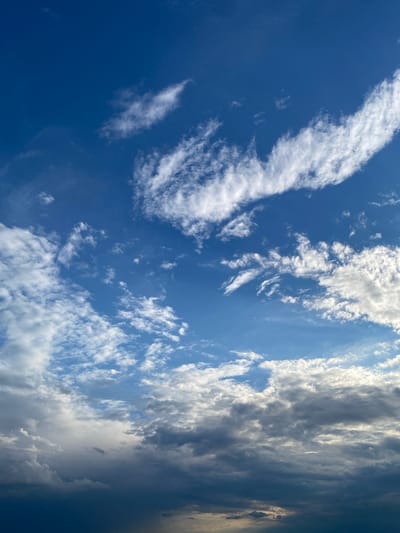 The image depicts a wide view of the sky above Horești, Moldova. The sky is a deep blue with varying cloud formations. In the upper portion of the image, wispy white clouds are scattered, appearing thin and feathery. Further down, the clouds become more dense and layered, with some exhibiting a greyish hue, suggesting depth and potentially approaching weather changes. The lower part of the sky is dominated by darker, heavier clouds, creating a dramatic contrast with the brighter sections above. The overall impression is of a dynamic sky, possibly at the transition of a day, with clear blue sky transitioning into more overcast conditions towards the horizon. No people, structures, or specific landmarks are visible in this sky-centric image.