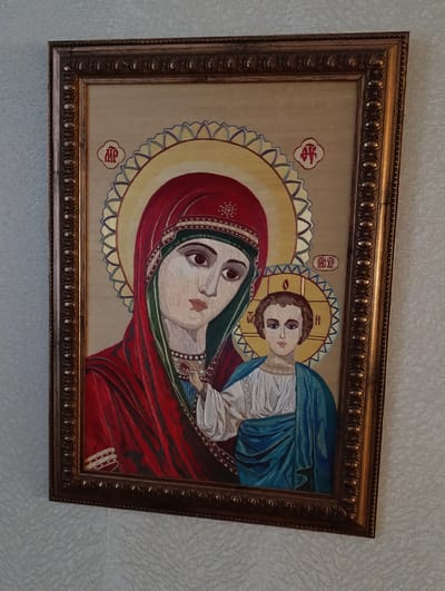 A framed image of the Virgin Mary and Jesus Christ hangs on a white wall. The image is a traditional religious icon. Mary is depicted wearing a red robe and head covering with green trim, while Jesus is shown in a blue and white robe. Both figures have halos around their heads. The frame is ornate and gold in color. There is no indication in the image as to the city of Barvinok, Ukraine.