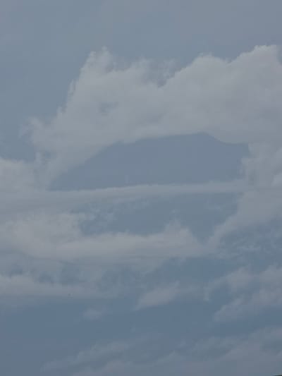The image shows a cloudy sky above Stanghella, Italy. The clouds are dense and gray, with some lighter patches suggesting sunlight breaking through. In the distance, the outline of a mountain range is faintly visible through the clouds, suggesting a possible elevation in the Stanghella area. There are no people, subjects, or objects clearly discernible within the frame of the image, focusing solely on the atmospheric conditions. The scene is neutral and devoid of any discernible activity, emphasizing a tranquil, natural environment.