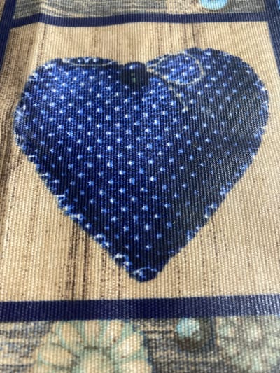 This media file is a close-up, high-angle shot of a textured fabric. The fabric features a repeating pattern of small, white dots on a dark blue background, forming a shape that resembles a stylized heart or a rounded arrowhead. This patterned element is set against a background of horizontal, beige threads, creating a woven appearance. To the left and right of the central pattern, there are vertical blue stripes and a section with a muted, abstract pattern in shades of blue and beige. The texture of the fabric is very prominent, with visible threads and a slightly rough surface. The lighting appears to be even, without strong shadows, suggesting an indoor setting or diffused daylight. No people, animals, or specific scenery are depicted. The image focuses entirely on the intricate details of the textile design and its material composition. The context provided, "Mitoc, Moldova," indicates the origin or location associated with this fabric, but the image itself offers no visual cues to confirm this. There is no visible text in the image.