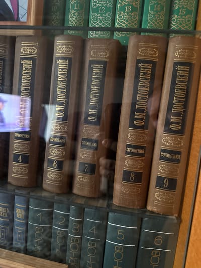 The image shows a bookshelf filled with books. The books are stacked horizontally and vertically, with their spines facing outward. The spines of many of the books display titles and author names in a foreign language, likely Russian, given the location context of Morozovka, Russia. Some books have dark green covers with gold lettering and ornate designs, while others have brown covers with similar gold embellishments. Visible text includes "Ф.М. ДОСТОЕВСКИЙ" and "СОЧИНЕНИЯ" on several spines, suggesting these are collected works of Fyodor Dostoevsky. Numbers such as "9", "8", "7", "6", "5", "4", "3", "2", "1", "12", "13", "14", and "15" are also visible, possibly indicating volume numbers. The lighting suggests an indoor setting, perhaps a library or a home with a well-stocked collection. The overall impression is one of order and intellectual pursuit, with the books arranged neatly on shelves. The image appears to have been taken at eye level, looking slightly upwards at the bookshelf. No people are visible in the frame. The scene is static, with no discernible activity.
--- OCR Start ---
EPH
BEPH
12
OPHOB
PHOB
4
6
7
8
PHOB
PHOBA
45
HOBO
OBの
Ф.М. ДОСТОЕВСКИЙ
Ф.М. ДОСТОЕВСКИЙ
СОЧИНЕНИЯ
СОЧИНЕНИЯ
СОЧИНЕНИЯ
СОЧИНЕНИЯ
СОЧИНЕНИЯ
6
12
13
Ф.М. ДОСТОЕВСКИЙ ||
Ф.М. ДОСТОЕВСКИЙ
--- OCR End ---