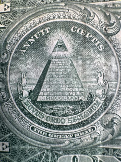 The image is a close-up, high-resolution photograph of the Great Seal of the United States, as depicted on a U.S. one-dollar bill. The design features an unfinished pyramid with an eye at its apex, surrounded by the Latin phrases "ANNUIT COEPTIS" above and "NOVUS ORDO SECTORUM" below. Roman numerals "MDCCLXXVI" are visible on the base of the pyramid. The intricate details of the engraving are clearly visible, including the texture of the paper and the fine lines of the design. There are no people, actions, or interactions depicted in the image. The environment is not a city, but rather the surface of currency. The location is not Mejaniga, Italy; it is a U.S. one-dollar bill.