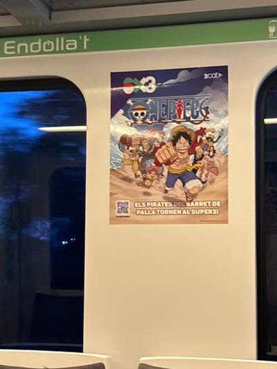 The image displays the interior of a public transport vehicle, likely a train or metro car, situated in Sant Quirze del Vallès, Spain. A large vertical poster, approximately half the width of the wall section, is affixed to a plain white interior panel. The poster features characters from the *One Piece* anime series; Monkey D. Luffy, wearing a straw hat, is central with his right fist extended, surrounded by other members of the Straw Hat Pirates. The *One Piece* logo is displayed at the top center of the poster, flanked by a "3x3" logo on the left and a "3cat" logo on the right. Below the character illustration, Catalan text reads "ELS PIRATES DEL BARRET DE PALLA TORNEN AL SUPERS3!" (The Straw Hat Pirates return to Supers3!), with a QR code in the bottom left corner. Above the poster, a horizontal green strip runs across the top of the interior space, bearing the white text "Endolla't" (Plug in yourself), indicating a charging facility. To the left of the poster, a rounded window displays a dark, blurred exterior view with faint, distant lights, consistent with a vehicle in motion during nighttime or dusk. Portions of grey upholstered seating are visible at the bottom of the frame.