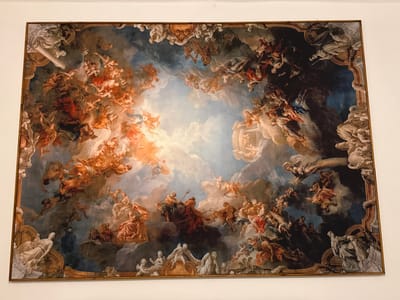 The image shows a framed painting depicting a scene of mythological figures set against a cloudy sky. The painting features numerous human figures, some of whom are partially clothed or nude, in various poses and groupings. The color palette is dominated by warm tones of orange, red, and brown, with contrasting areas of blue and grey. The frame is ornately decorated. The painting is located at the Galleria Nazionale dell'Umbria, Perugia, Italy.