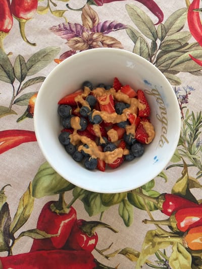 The image depicts a white bowl filled with strawberries and blueberries, drizzled with a brown sauce, possibly peanut butter or tahini. The bowl has the word "gongolo" inscribed on it. It sits on a patterned tablecloth featuring images of peppers, leaves, and flowers. The image appears to be taken from directly above the bowl.

There is no information in the image to suggest a location in Lissone, Italy.