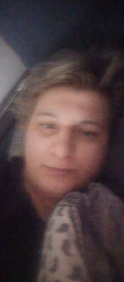 The image shows a close-up, blurry, and dimly lit selfie of a person lying down and looking towards the camera. The person has light-colored hair and their face is partially obscured by what appears to be a patterned blanket or clothing. The background is dark and indistinct, suggesting an indoor setting at night or in low light. No specific details of the city of Saburovo, Russia, are visible in the image.