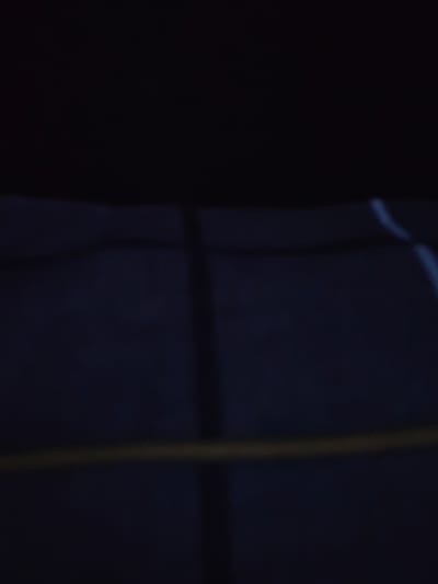 The image is a dimly lit, abstract, and blurry depiction of what appears to be a dark blue textured surface. A horizontal yellow-toned line runs across the middle of the frame, potentially representing a string or a light source. Faint vertical shadows are also visible, suggesting some form of obstruction or structure casting them. The overall impression is one of low light conditions, possibly at night or in a very dark indoor environment. There is no discernible text, people, or specific objects, making it difficult to determine the exact scene or activity. The context of Ishim, Russia, does not provide any immediate clues to interpret the abstract elements within the image.