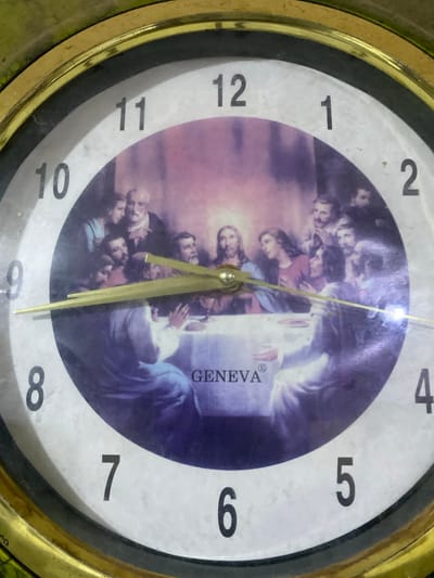 The image shows a close-up of a wall clock. The clock face features a painting of "The Last Supper" with Jesus and his disciples. The numbers 1 through 12 are visible around the clock face. The clock hands are visible and point to approximately 4:08. The clock has a gold-colored frame and is mounted on a wall in an indoor setting. There is no information in the image to suggest its location in Jere South, Nigeria.